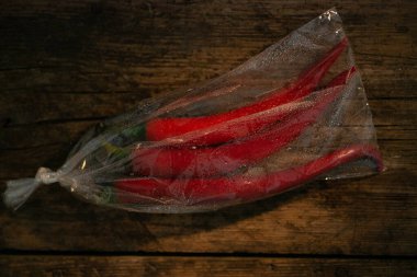 Ahşap bir arka planda plastik bir pakette kırmızı biber. Üç büyük biber..