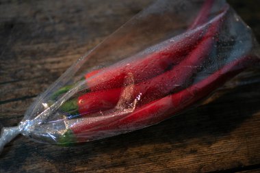Ahşap bir arka planda plastik bir pakette kırmızı biber. Üç büyük biber..