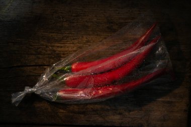 Ahşap bir arka planda plastik bir pakette kırmızı biber. Üç büyük biber..