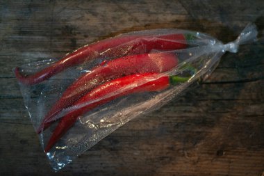 Ahşap bir arka planda plastik bir pakette kırmızı biber. Üç büyük biber..
