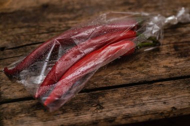 Ahşap bir arka planda plastik bir pakette kırmızı biber. Üç büyük biber..