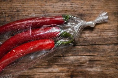 Ahşap bir arka planda plastik bir pakette kırmızı biber. Üç büyük biber..