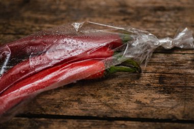 Ahşap bir arka planda plastik bir pakette kırmızı biber. Üç büyük biber..