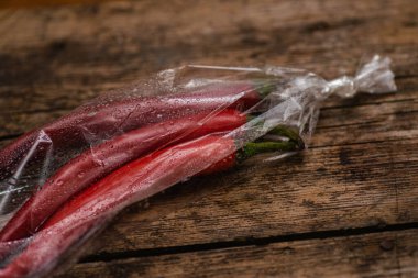 Ahşap bir arka planda plastik bir pakette kırmızı biber. Üç büyük biber..