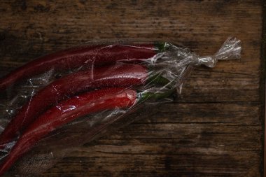 Ahşap bir arka planda plastik bir pakette kırmızı biber. Üç büyük biber..