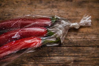 Ahşap bir arka planda plastik bir pakette kırmızı biber. Üç büyük biber..