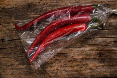 Ahşap bir arka planda plastik bir pakette kırmızı biber. Üç büyük biber..