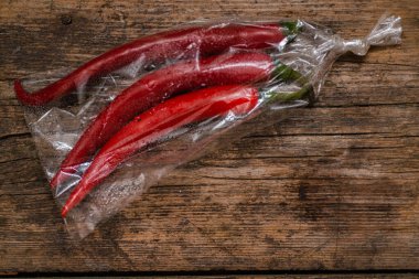 Ahşap bir arka planda plastik bir pakette kırmızı biber. Üç büyük biber..