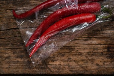 Ahşap bir arka planda plastik bir pakette kırmızı biber. Üç büyük biber..