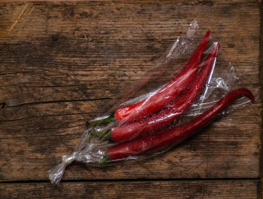 Ahşap bir arka planda plastik bir pakette kırmızı biber. Üç büyük biber..