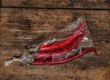 Ahşap bir arka planda plastik bir pakette kırmızı biber. Üç büyük biber..