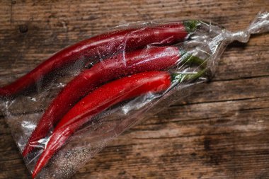 Ahşap bir arka planda plastik bir pakette kırmızı biber. Üç büyük biber..