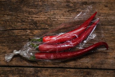 Ahşap bir arka planda plastik bir pakette kırmızı biber. Üç büyük biber..