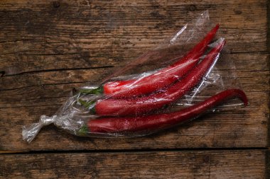 Ahşap bir arka planda plastik bir pakette kırmızı biber. Üç büyük biber..