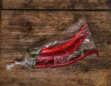 Ahşap bir arka planda plastik bir pakette kırmızı biber. Üç büyük biber..
