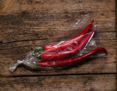 Ahşap bir arka planda plastik bir pakette kırmızı biber. Üç büyük biber..