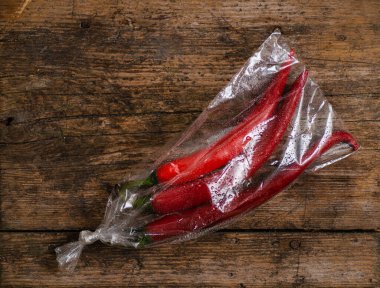 Ahşap bir arka planda plastik bir pakette kırmızı biber. Üç büyük biber..