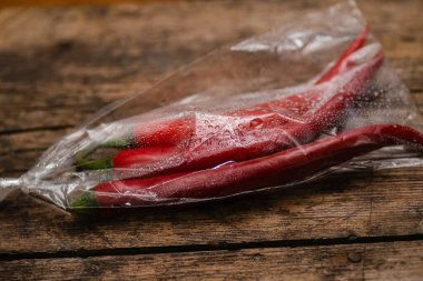 Ahşap bir arka planda plastik bir pakette kırmızı biber. Üç büyük biber..