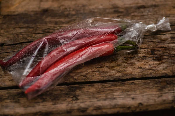 Ahşap bir arka planda plastik bir pakette kırmızı biber. Üç büyük biber..