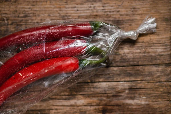 Ahşap bir arka planda plastik bir pakette kırmızı biber. Üç büyük biber..