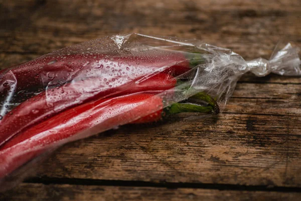 Ahşap bir arka planda plastik bir pakette kırmızı biber. Üç büyük biber..