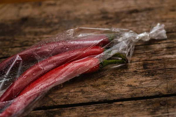 Ahşap bir arka planda plastik bir pakette kırmızı biber. Üç büyük biber..