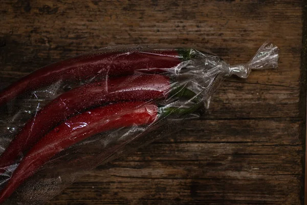 Ahşap bir arka planda plastik bir pakette kırmızı biber. Üç büyük biber..