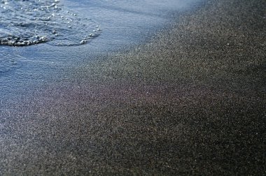 Deniz kıyısındaki siyah volkanik manyetik kum. Sahilin arka planında dalgalar birbirine yakın.. 