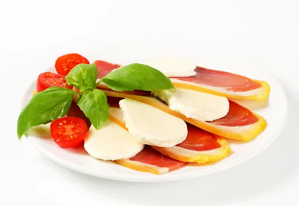 Sliced prosciutto and mozzarella with basil and tomatoes — Stock Photo, Image