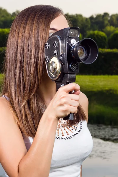 Chica joven usando una cámara de cine a la antigua en un parque — Foto de Stock