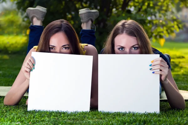 Glada unga tjejer hålla vit blank papper mot bakgrund — Stockfoto