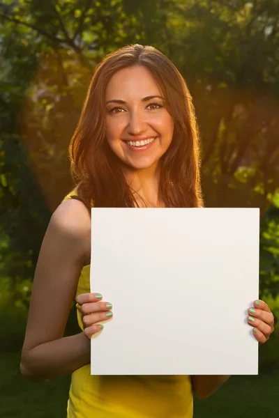 Glada leende ung flicka håller vitt blankt papper — Stockfoto