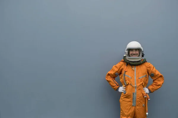 Astronaut na sobě oranžový kosmický oblek a vesmírná helma s úsměvem při pózování proti šedé zdi pozadí — Stock fotografie