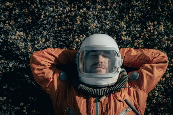 Gros plan d'un cosmonaute portant une combinaison spatiale et un casque spatial faisant une sieste tout en étant allongé sur de l'herbe à l'extérieur. Portrait d'un astronaute dormant sur une prairie — Photo