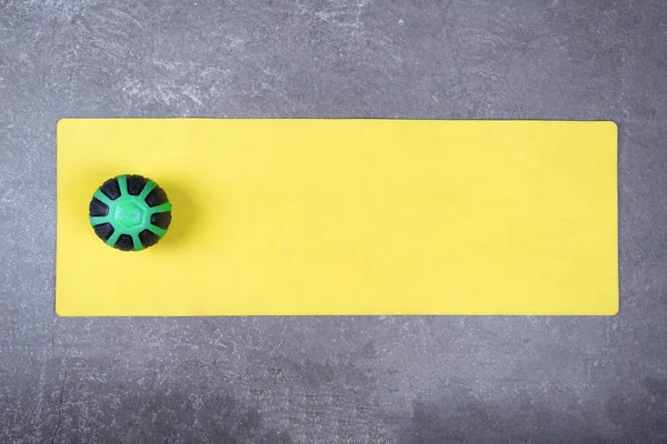 Pose plate de tapis de yoga jaune avec boule médicale sur le sol en béton. Med ball sur tapis de fitness étalé sur le sol de ciment — Photo