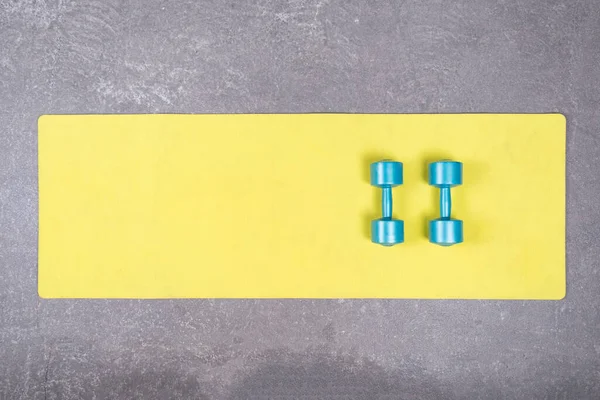 Flat lay of two dumbbells on yelow fitness mat on concrete floor. Dumbbells on fitness mat spread out on cement floor — Stock Photo, Image