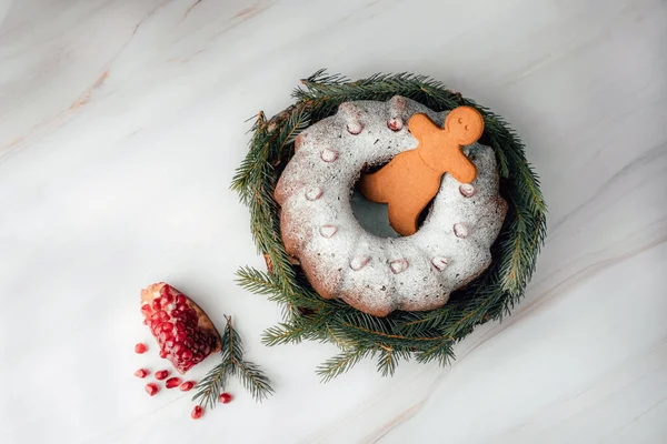Piernikowy mężczyzna zagnieżdżony w świąteczny tort z granat na marmurowy stół tło. Ciasto świąteczne z lukrem i dekoracji świątecznej. — Zdjęcie stockowe