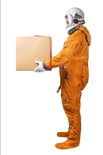 Űrhajós narancssárga űrruhát és űrsisakot visel, kezében barna kartondobozban, fehér alapon elkülönítve. Szállítási koncepció. — Stock Fotó