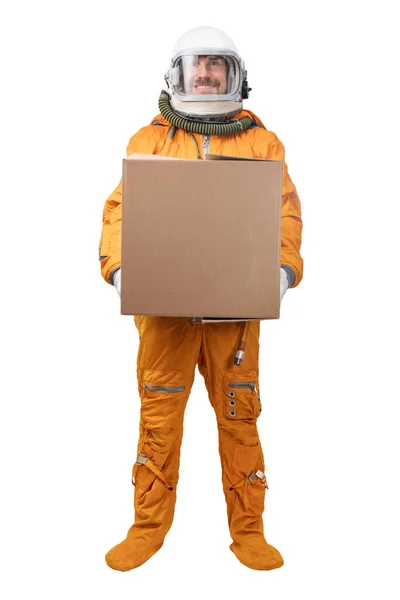 Астронавт в оранжевом скафандре и космическом шлеме держит в руке пустой квадратный картонный ящик, изолированный на белом фоне — стоковое фото