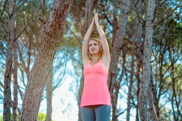 Счастливая молодая женщина практикует йогу с поднятыми вверх руками в лесу. Поза восходящего салюта — стоковое фото