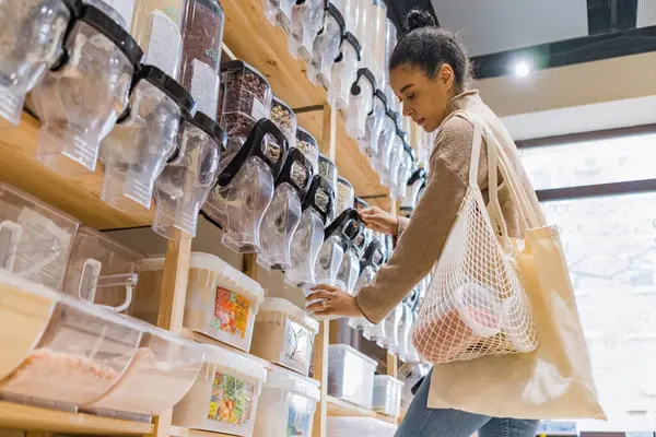 Giovane donna afroamericana mascherata che compra cereali e cereali in un supermercato sostenibile a zero rifiuti — Foto Stock