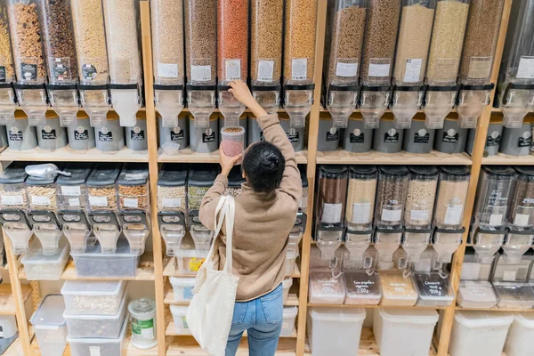 Молодая африканская американка покупает органические крупы и зерно в устойчивом продуктовом магазине нулевых отходов. Вид сзади Лицензионные Стоковые Изображения