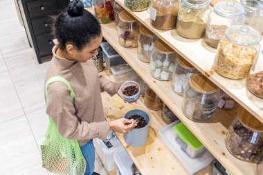 Genç Afrikalı Amerikalı kadın sürdürülebilir sıfır atık marketten organik çay alıyor. Genç bir kadın tekrar kullanılabilir konteynırı yerel bir markette çayla dolduruyor.