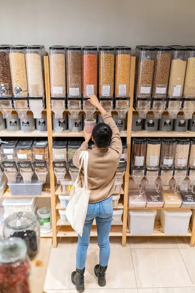 Mladá africká Američanka kupuje bezlepkové těstoviny v udržitelném obchodě s potravinami s nulovým odpadem. Mladá žena plnící opakovaně použitelný kontejner s těstovinami v místním obchodě. — Stock fotografie