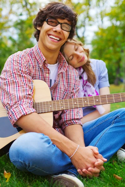 Cheerful teenage couple with guitar in park — Stock Photo, Image