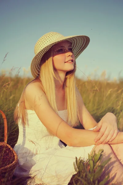 Young girl in straw hat sitting in field — Stock Photo, Image