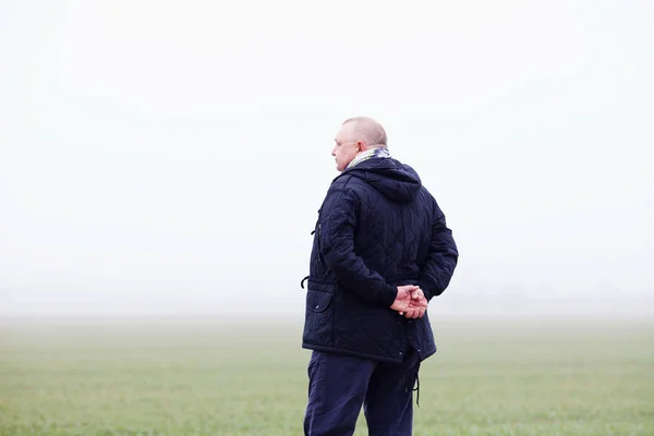 Uomo anziano in campo nebbioso da dietro — Foto Stock