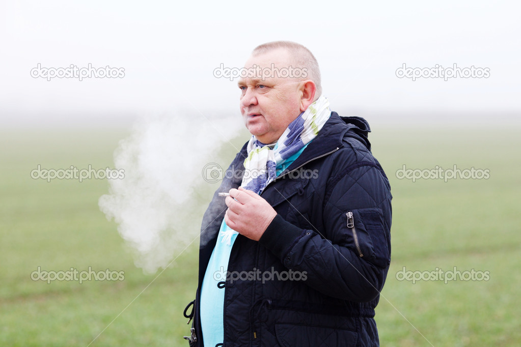 Senior man smoking over foggy field