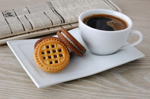 Una taza de café y galletas y un periódico — Foto de Stock