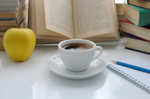 Una taza de café y una manzana sobre una mesa entre libros — Foto de Stock